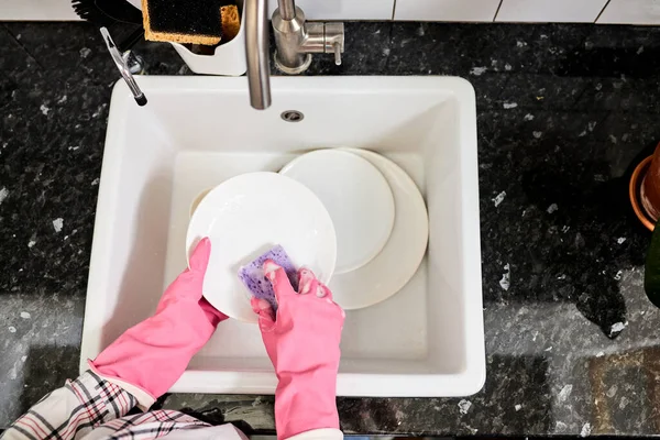 Vista superior de las manos femeninas en guantes enjuagar los platos con esponja púrpura por encima del fregadero de la cocina —  Fotos de Stock