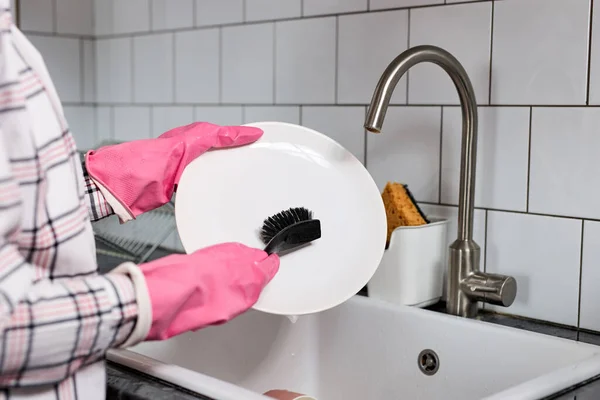 Foto de cerca de las manos femeninas en guantes de goma rosa lavando el plato con cepillo de platos — Foto de Stock