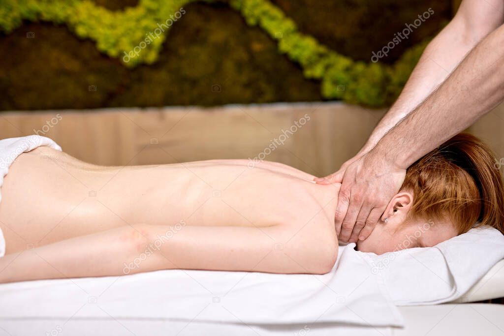 Young beautiful woman lying on massage table and enjoying massage by professional