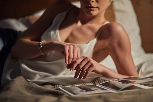 Mjuk och elegant beskärd kvinna med kort elegant hår ligger på sängen med tidningen bilder — Stockfoto