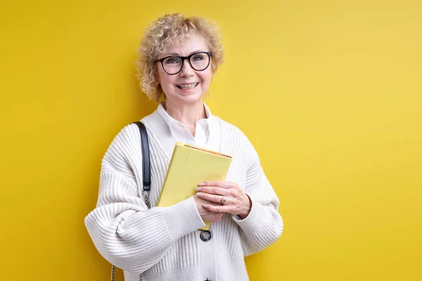 Usmívající se stařena drží knihu v rukou, nosí brýle, sebevědomý učitel — Stock fotografie