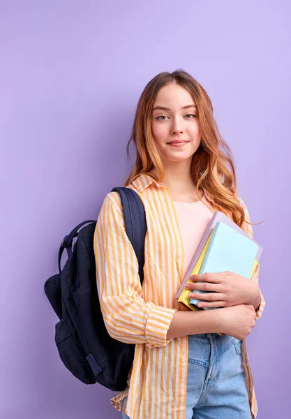 Caucásico chica adolescente estudiante en casual desgaste con mochila y libros aislados en púrpura fondo estudio retrato, mira la cámara — Foto de Stock