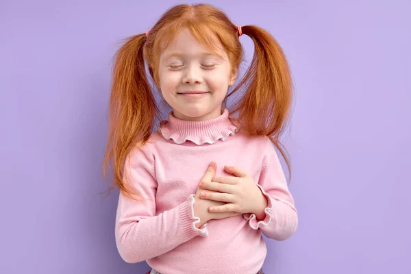 Trevlig rödhårig flicka som håller händerna på bröstet, känner tacksamhet eller drömmer — Stockfoto