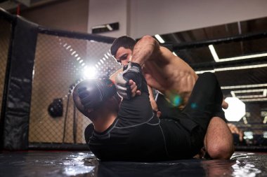 Güçlü bir MMA dövüşçüsü spor salonunda paspas üzerinde rakibini yumrukluyor, kuralsız dövüş sırasında.