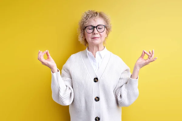 Starší žena v brýlích zachovat klid, namaste, izolované přes žluté pozadí — Stock fotografie