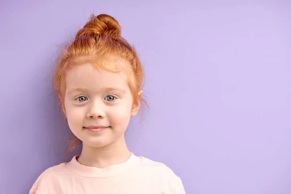 Close-up portrait of cute smiling caucasian child girl with red hair and big blue eyes isolated over purple background — Stock Photo, Image