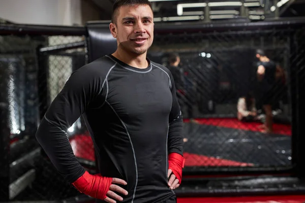 Homem positivo no ringue em ligaduras de boxe vermelho se preparando para a batalha, sorrindo para a câmera — Fotografia de Stock