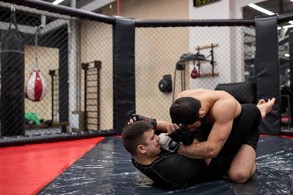 Shirtloze sterke mma vechter in bokshandschoenen zittend boven tegenstander terwijl sportman liggend op vloer weerstand biedt — Stockfoto