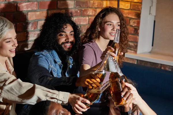 Diverse vrienden hebben kleine home party, vergadering, zitten op de bank, klappen flessen bier — Stockfoto