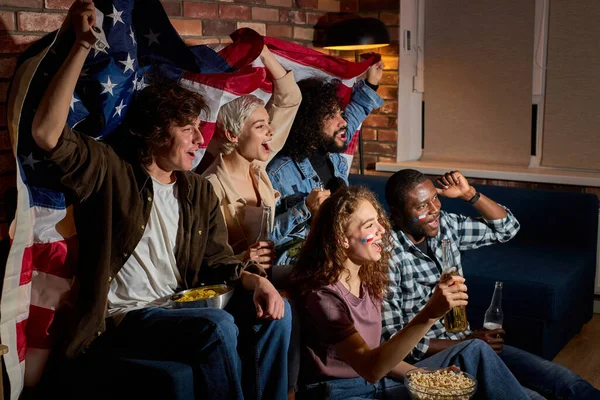Veselý multikulturní američtí přátelé fotbalových fanoušků se shromáždili doma v tmavé místnosti sledování v televizi sportovní hry — Stock fotografie