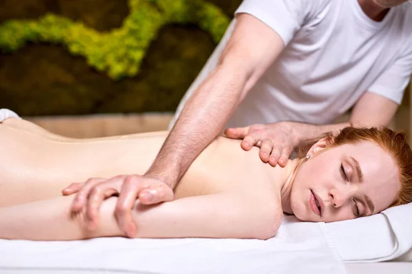 Irriconoscibile terapeuta maschile massaggio rossa donna attraente, vista laterale — Foto Stock