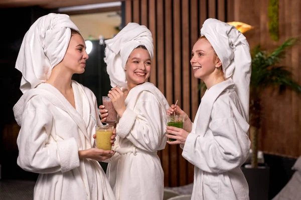 Trois jolies copines boivent une boisson juteuse et bavardent animément tout en se relaxant dans le salon de spa — Photo