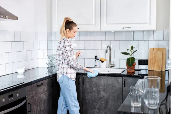 Femme au foyer concentrée nettoyage de la table de cuisine et évier avec chiffon bleu caillot. — Photo