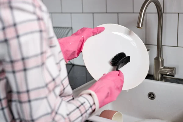 Foto de cerca de las manos femeninas en guantes de goma rosa lavando el plato con cepillo de platos —  Fotos de Stock