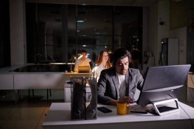 Yöneticilerin ofis çalışanları bilgisayar kullanarak geç saatlere kadar proje üzerinde çalışıyorlar.