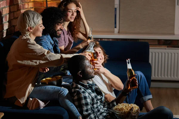 Grupo interracial de amigos que tienen una pequeña fiesta en casa, reunión, sentarse en el sofá, botellas de cerveza — Foto de Stock