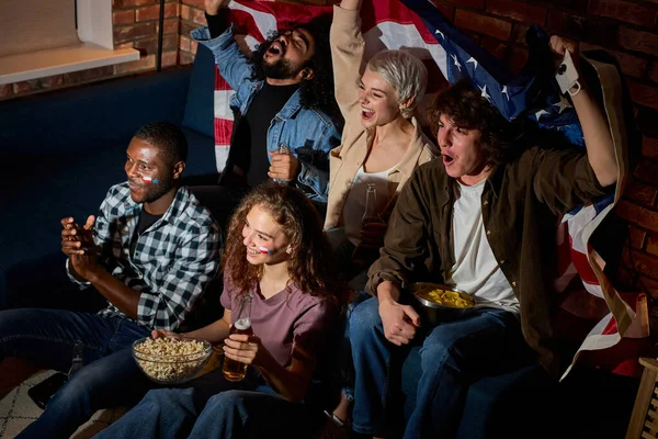 Emocionados amigos americanos multiculturales aficionados al fútbol se reunieron en casa en la habitación oscura viendo en la televisión juego deportivo — Foto de Stock