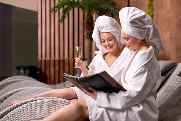 Girlfriends in bath towels communicating in spa salon while drinking champagne — Zdjęcie stockowe