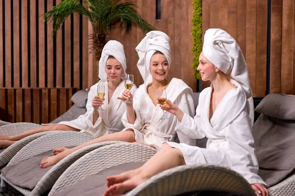 Чудові жінки в халатах і рушниках насолоджуються відпочинком у спа-центрі, п'ють шампанське — стокове фото