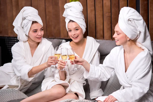 Happy females in bathrobes and towels enjoying holidays in spa center, drinking champagne — стоковое фото