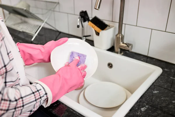 Foto de cerca de las manos femeninas lavándose el plato blanco con esponja y espuma en el fregadero de la cocina — Foto de Stock