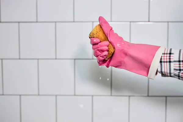 Guante de mano en goma que sostiene la esponja, aislado en la pared de azulejos blancos —  Fotos de Stock