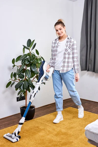 Mujer joven caucásica que usa ropa casual limpiando el piso de la casa en la sala de estar usando aspiradora moderna —  Fotos de Stock