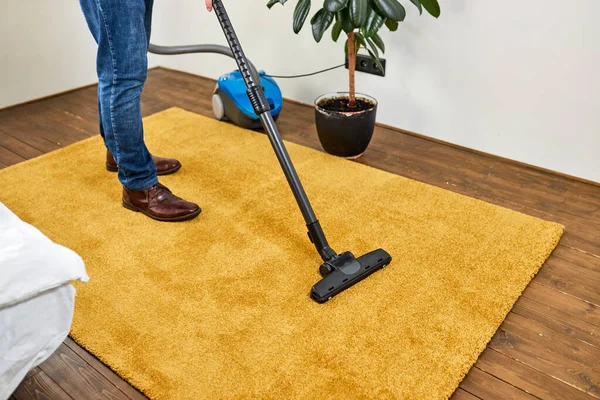 Cropped man in casual wear vacuum cleaning yellow carpet, tidying white modern living room. Home, housekeeping concept — стоковое фото