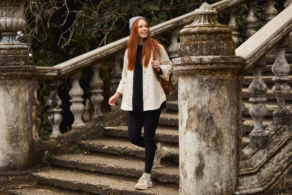 Female traveler goes down the stairs of ancient building, looking away in contemplation — Zdjęcie stockowe