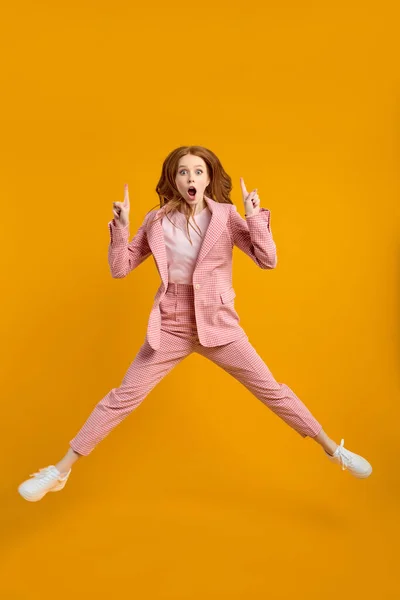 Business lady jumping with raised fingers showing up isolated on yellow background — Stock Photo, Image