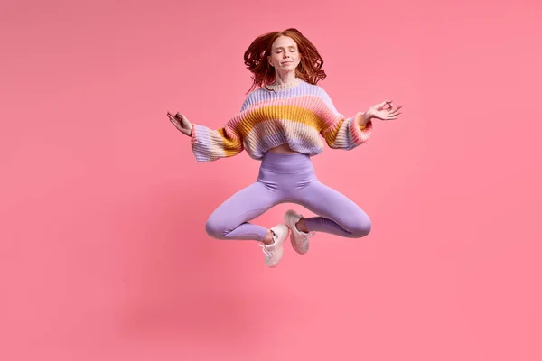 Beautiful redhead lady jumping high sitting air in lotus pose practicing morning yoga — стоковое фото