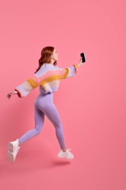 Tozluklu kızıl saçlı kadın portresi akıllı telefonuyla ileri doğru atlıyor.