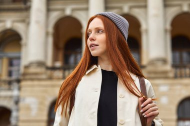 Kızıl saçlı kadın ziyaretçi eski bir yerden geçiyor, tarihi bölgeyi keşfediyor.