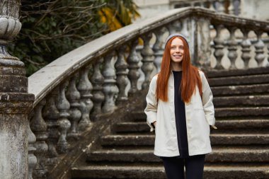 Kızıl saçlı kadın ziyaretçi eski bir yerden geçiyor, tarihi bölgeyi keşfediyor.