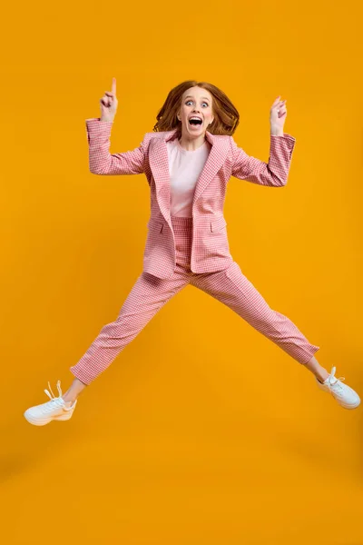 Aufgeregte Frau springt mit erhobenen Fingern auf gelbem Hintergrund — Stockfoto