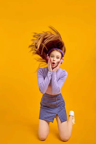 Эмоциональные молодые счастливые сумасшедшие женщины в наушниках с летящими волосами изолированы на желтый — стоковое фото