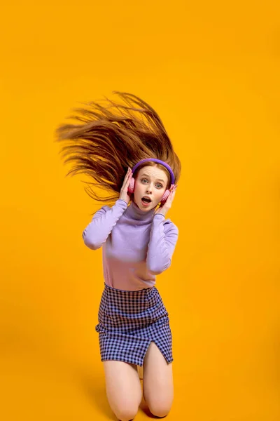 Эмоциональные молодые счастливые сумасшедшие женщины в наушниках с летящими волосами изолированы на желтый — стоковое фото