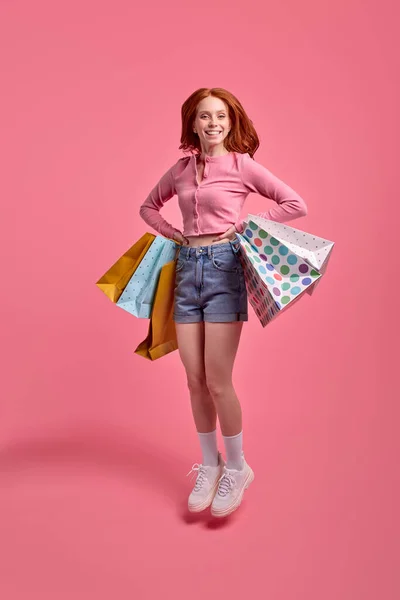 Красивая рыжеволосая молодая забавная забавная леди наслаждается покупками, держа пакеты — стоковое фото