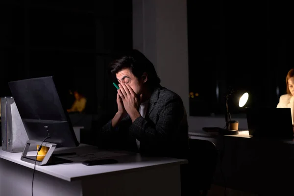 Kaukázusi barna férfi öltönyben ül éjszaka az irodában, szeme fáj a túlterheltség — Stock Fotó