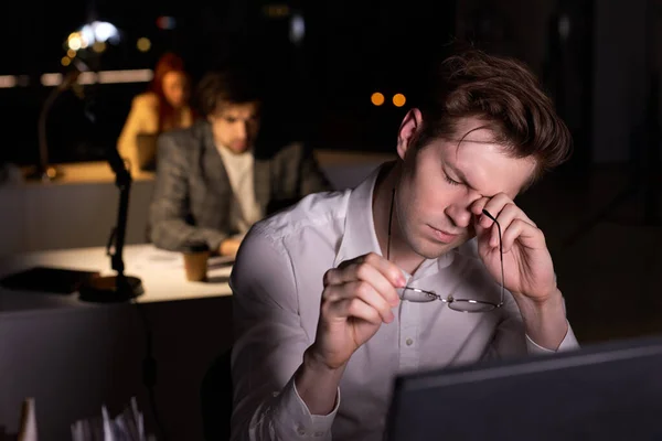 Νεαρός Καυκάσιος με επίσημη ένδυση που έχει χρόνια εργασιακή κούραση, στο γραφείο τη νύχτα — Φωτογραφία Αρχείου