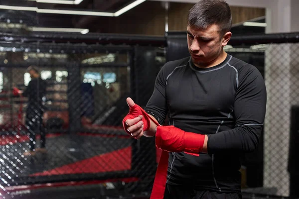 Lutador de Kickboxer masculino caucasiano confiante que se prepara para a luta, mão de embrulho em bandagem vermelha — Fotografia de Stock