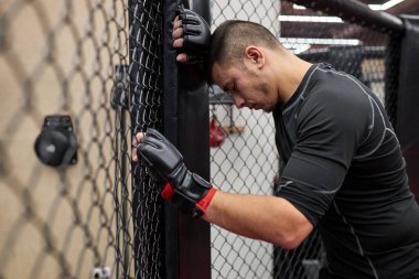 Spor salonunda sıkı çalıştıktan sonra kafese dayanan yorgun genç adamın portresi.