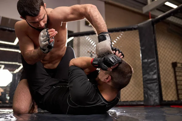 Shirtless forte lutador mma em luvas de boxe sentado acima do adversário, enquanto desportista deitado no chão resistindo — Fotografia de Stock