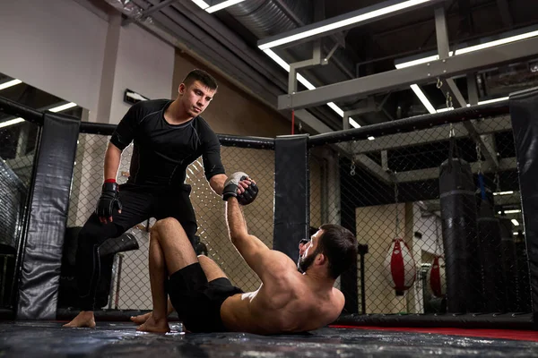 Vista lateral de artistas marciales mixtos durante la pelea, ayudarse mutuamente, en el ring en el gimnasio —  Fotos de Stock