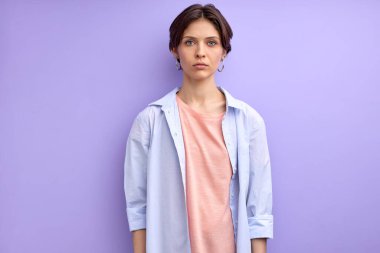 Gündelik gömlekli ciddi bir beyaz kadın kameraya bakıyor, sakin ve kendinden emin.