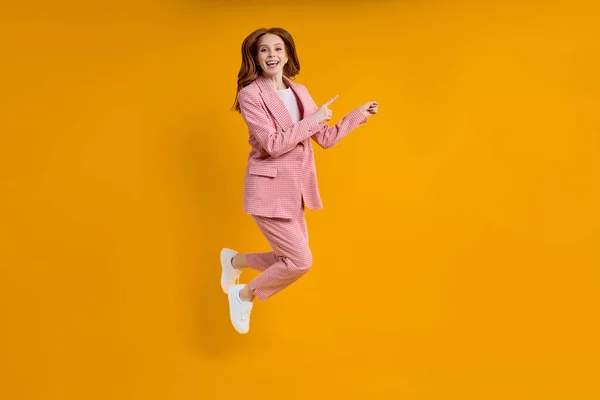 Erfolgreiche Geschäftsfrau im Anzug springt mit erhobenem Zeigefinger zur Seite, isoliert auf gelbem Hintergrund — Stockfoto