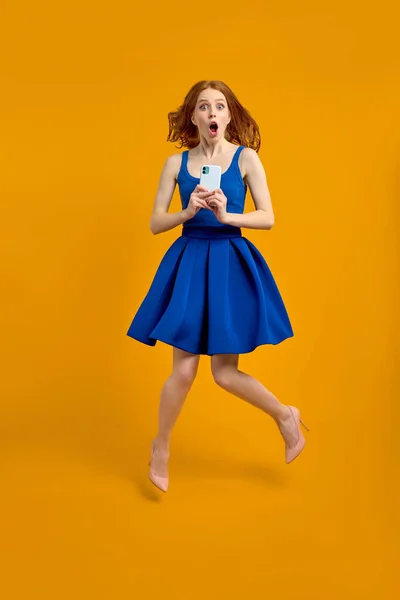 Retrato de dama pelirroja conmocionada en vestido saltando alto sosteniendo el teléfono — Foto de Stock