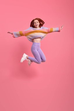 Heyecanlı, sıradan giyinmiş, kollarını açarak atlayan, izole bir genç bayan.