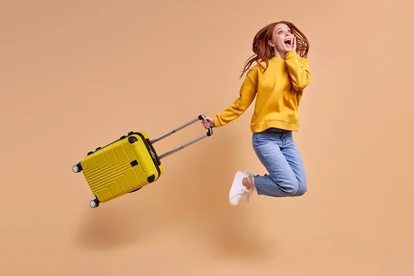 Excited beautiful redhead woman is going to have vacation jumping with cabin bag — Stock Photo, Image