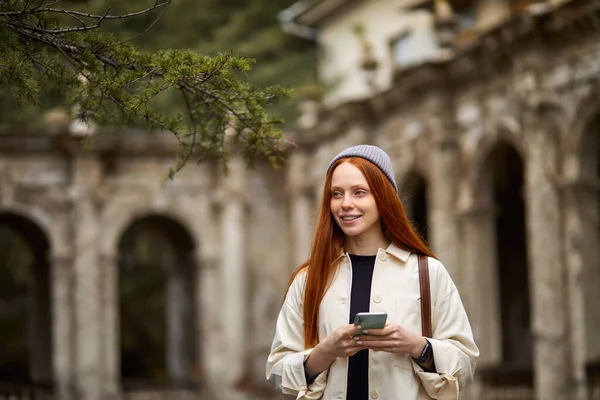 Porträtt av vacker kvinna står bredvid gamla byggnaden med modern smartphone — Stockfoto